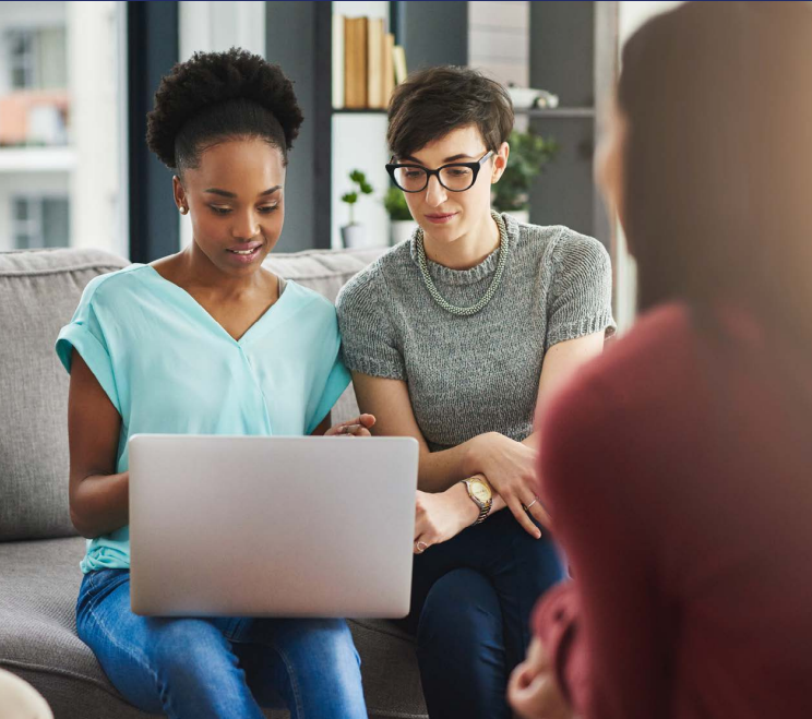 two women looking over a laptop with another looking on