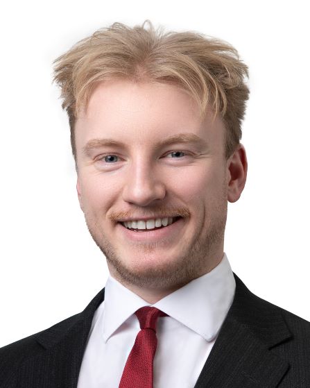 Mitchell Kubrak headshot. He has reddish blonde hair and is wearing a dark suit and red tie.