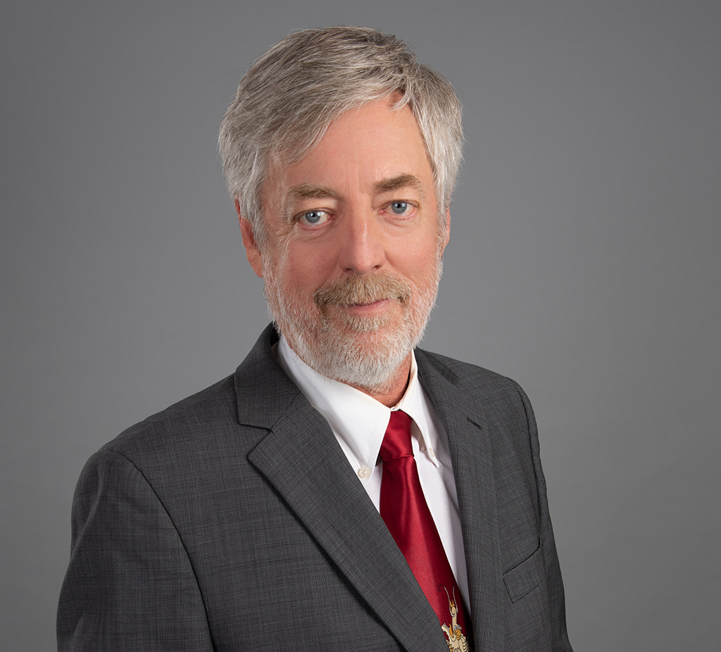 Shawn Brayman headshot. He is wearing a dark grey suit with a red tie.