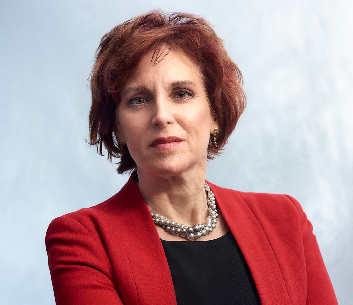 Tashia Batstone headshot. She is wearing a red blazer and looking confidently at the camera