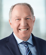 Ron Harvey is wearing a dark blue suit, striped tie and is smiling warmly at the camera